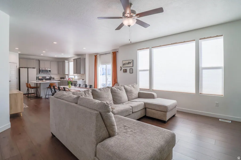Open-concept living area featuring wood-finish flooring, a ceiling fan with integrated lighting, and multiple large windows