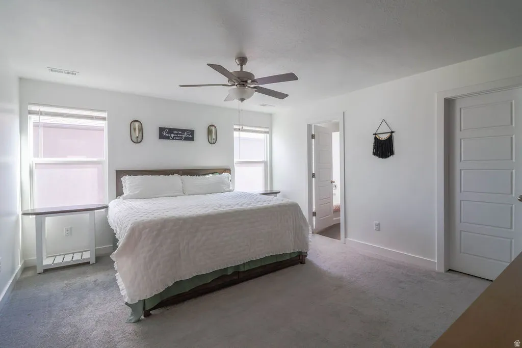 Spacious room with light gray carpeting, a ceiling fan with light fixture, and two large windows