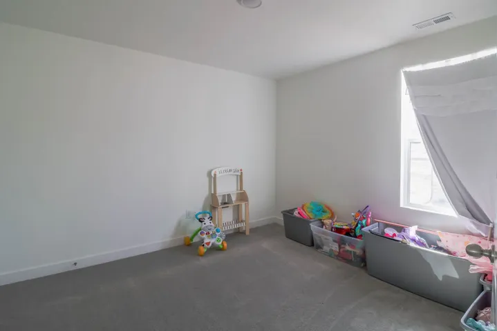 Recessed ceiling lighting, white painted walls, gray carpet flooring, and a single window with a white frame