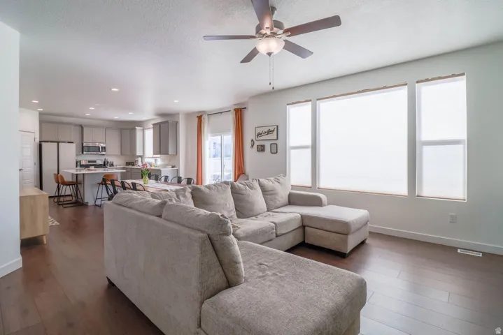 Open-concept living area featuring wood-finish flooring, a ceiling fan with integrated lighting, and multiple large windows