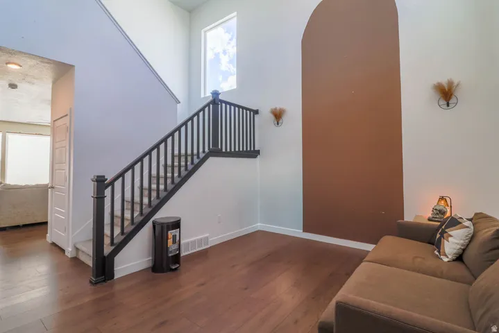 Hardwood-finish flooring, staircase with dark wood-finish balusters, vaulted ceiling, and a prominent arched wall detail