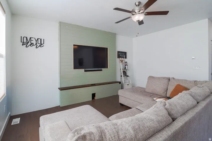 Wood-finish flooring, accent wall with built-in media console, ceiling fan with integrated lighting