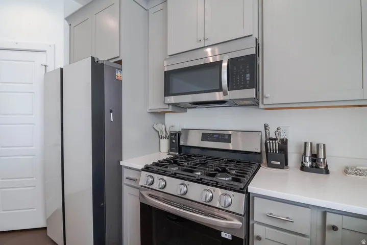 Stainless steel range with gas cooktop, stainless steel microwave, light gray cabinetry, and white countertops