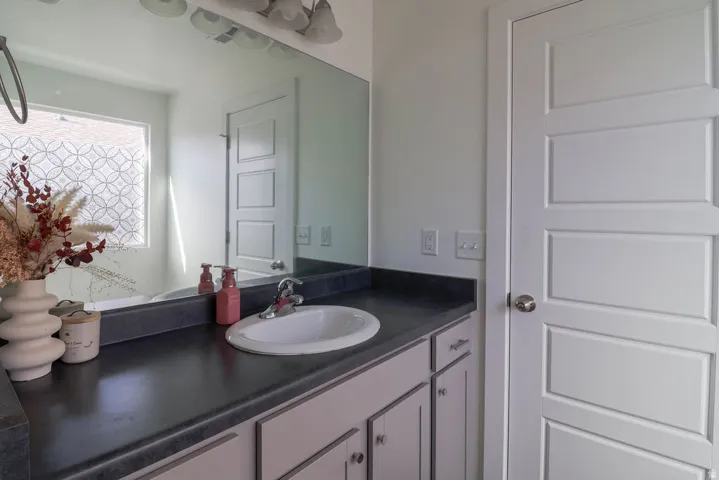 White panel door, vanity with a dark countertop, integrated sink, and wall-mounted mirror