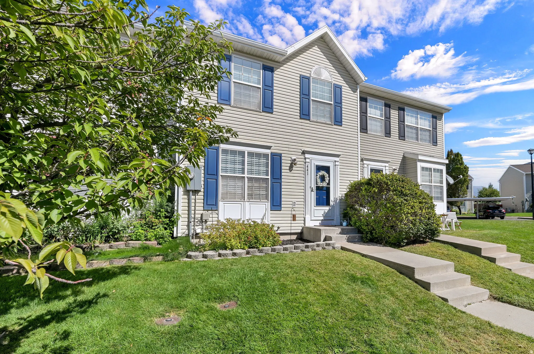 Vinyl siding exterior with blue window shutters, concrete walkways, and landscaped planting beds