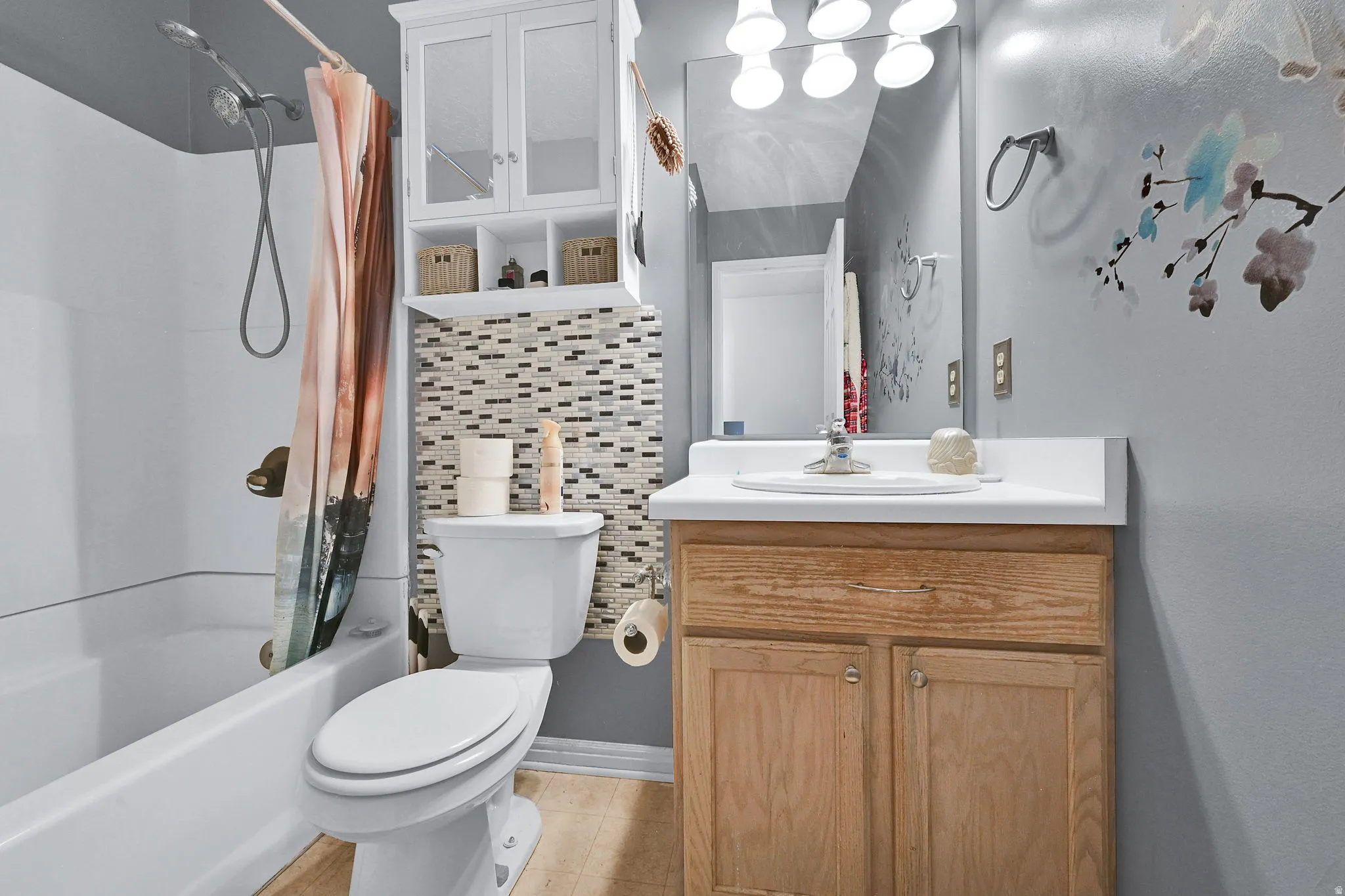 Full bathroom featuring a white tub-shower combination, a toilet with a mosaic tile accent wall, a wood-finish vanity with an integrated sink, and an overhead mirrored medicine cabinet
