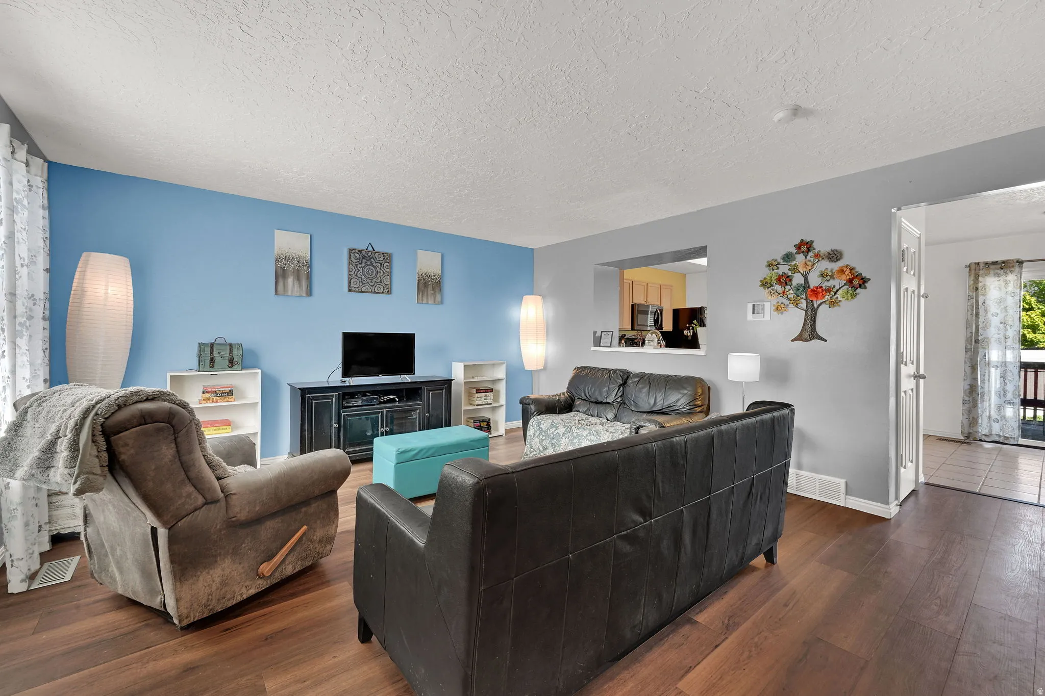 Wood-finish flooring throughout, light blue and gray wall tones, and a pass-through window to an adjacent room