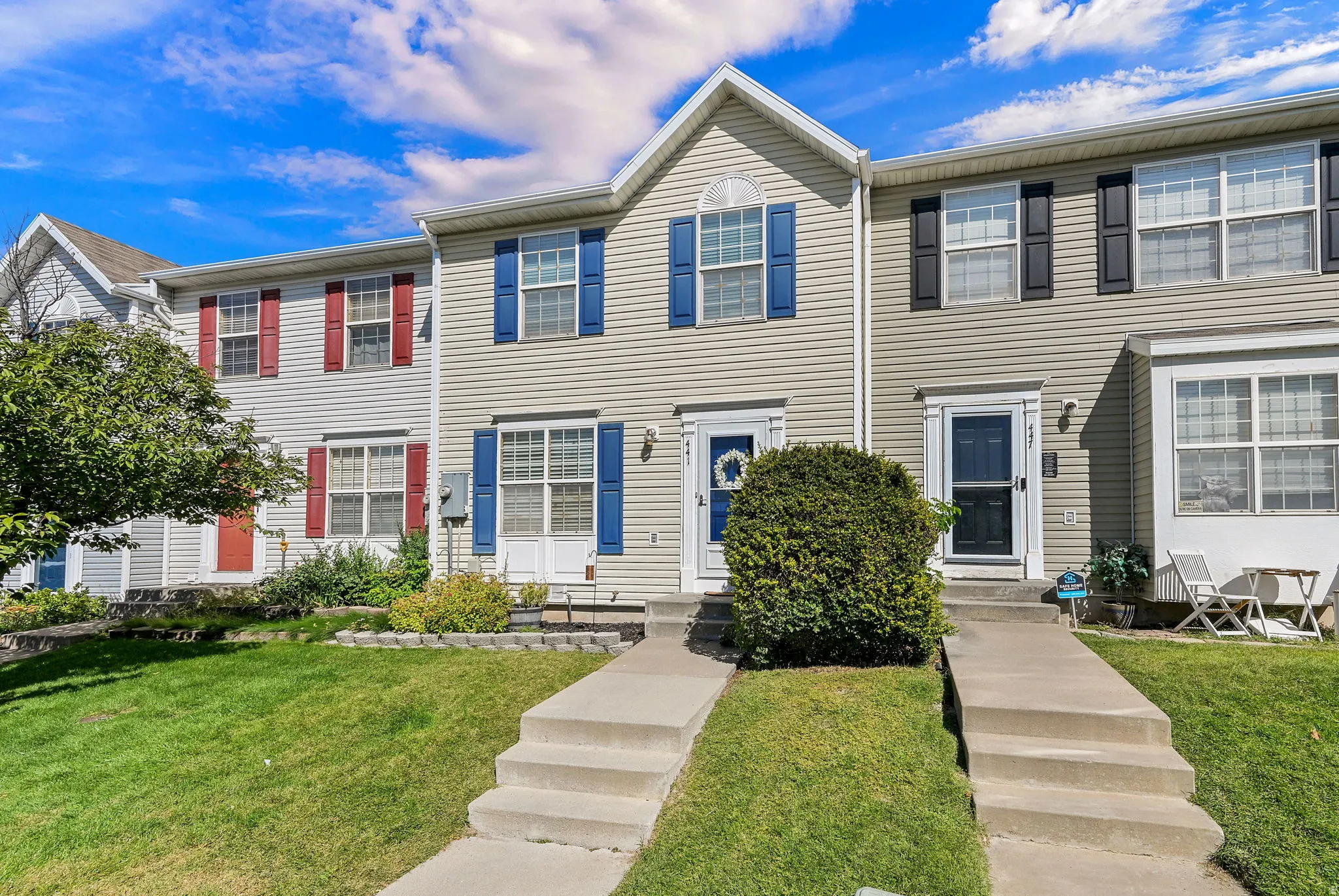 Townhome exterior featuring vinyl siding, contrasting shutters, concrete walkways, and a manicured lawn