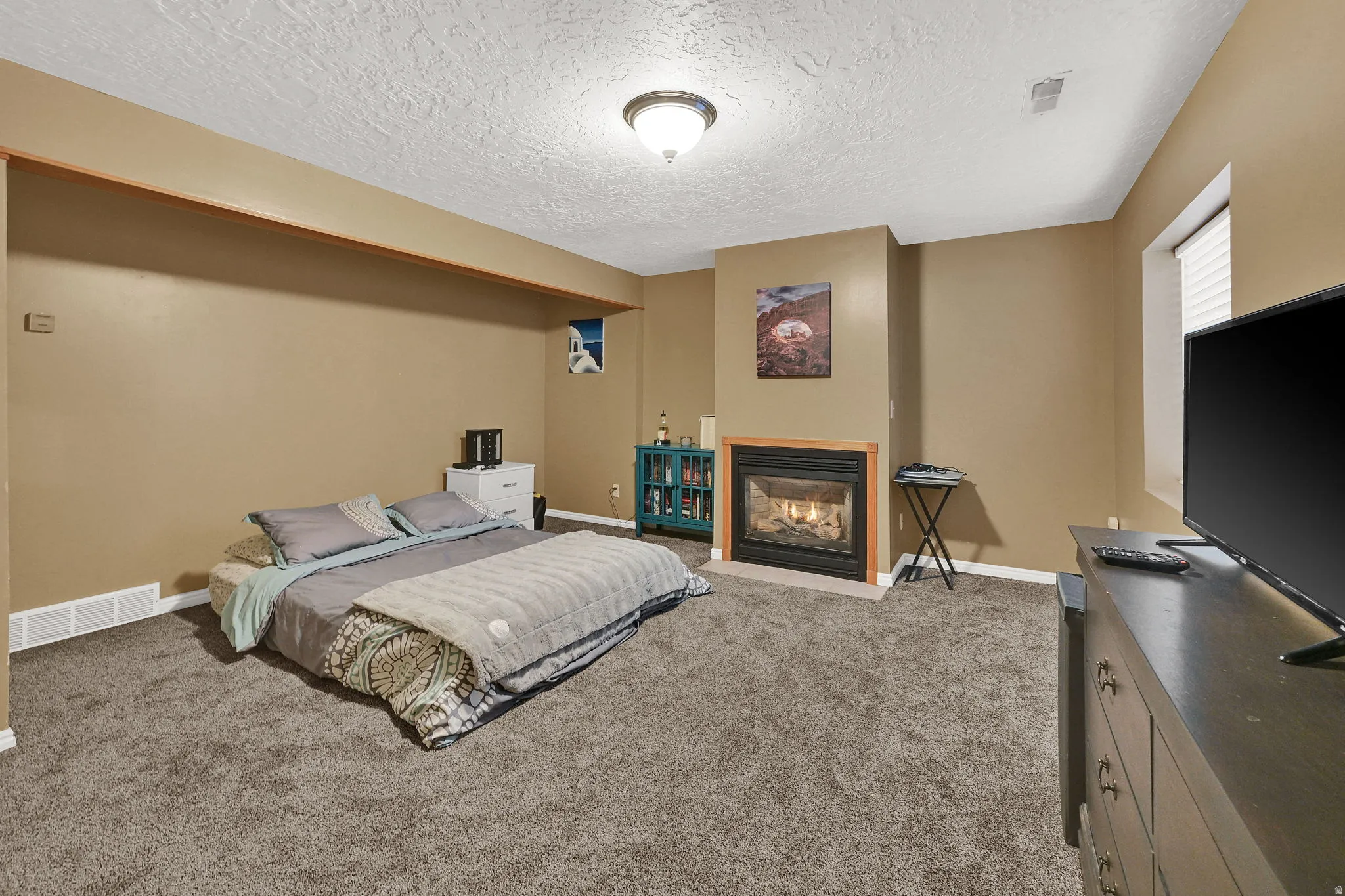 Carpeted room featuring a built-in fireplace with a tile surround and wood mantel, a window with horizontal blinds, and a flush mount ceiling light fixture