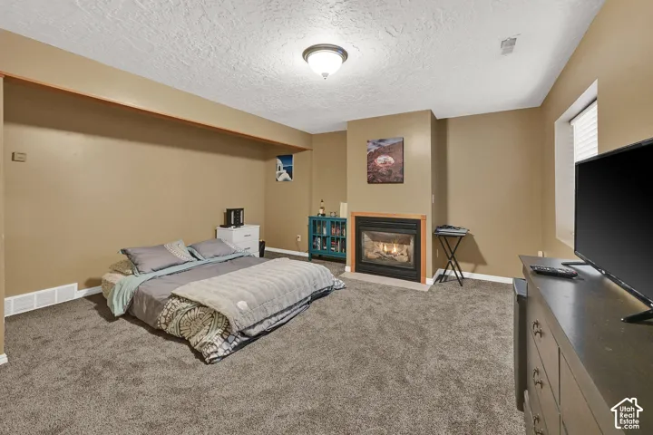 Carpeted room featuring a built-in fireplace with a tile surround and wood mantel, a window with horizontal blinds, and a flush mount ceiling light fixture