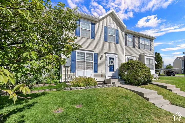Vinyl siding exterior with blue window shutters, concrete walkways, and landscaped planting beds