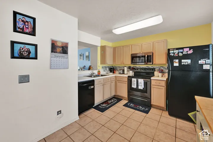 Kitchen featuring light wood-finish cabinetry, tile flooring, black appliances, and a mosaic tile backsplash