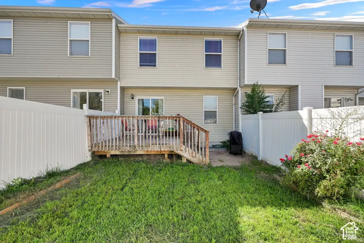 Wood deck with railing, white vinyl fencing, sliding glass door access, light-colored siding, and a landscaped shrub
