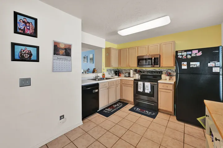 Kitchen featuring light wood-finish cabinetry, tile flooring, black appliances, and a mosaic tile backsplash