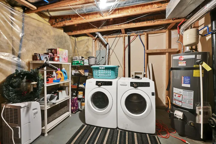 Unfinished basement space featuring a water heater, exposed wood joists, and laundry hookups