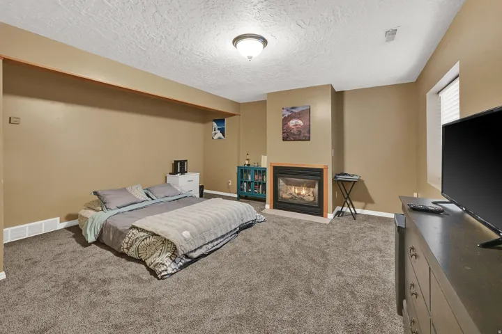 Carpeted room featuring a built-in fireplace with a tile surround and wood mantel, a window with horizontal blinds, and a flush mount ceiling light fixture