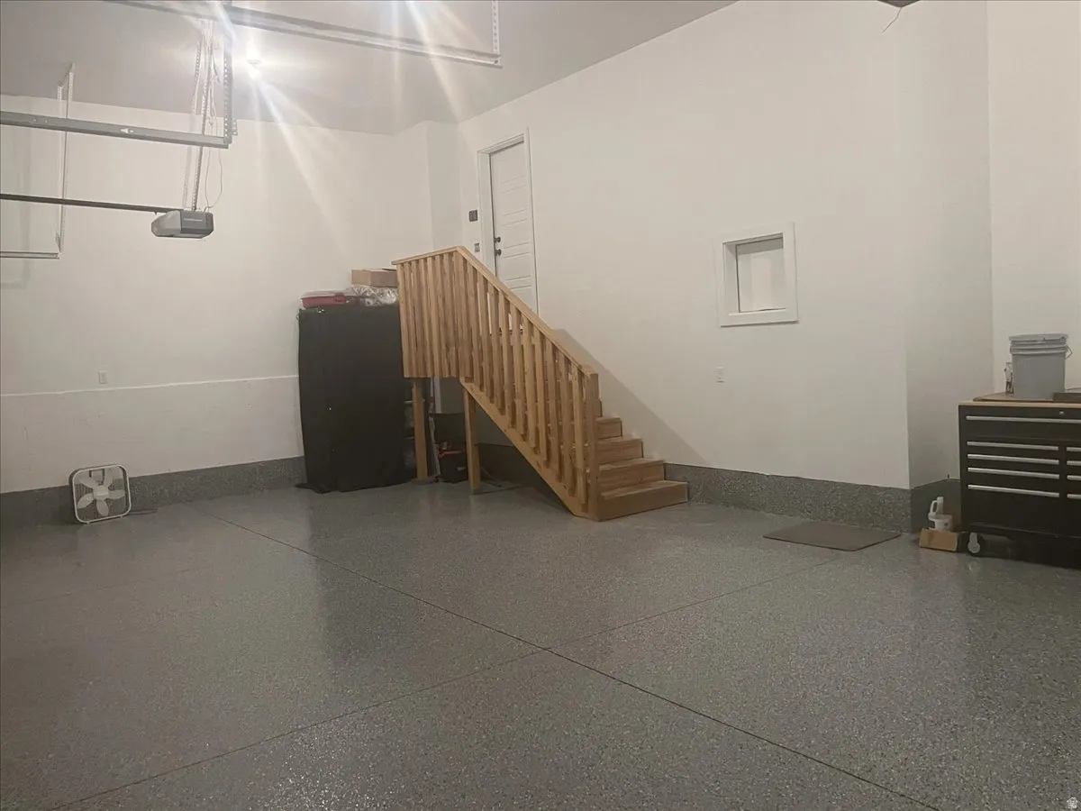 Spacious garage with light gray speckled flooring, white walls, and a natural wood staircase