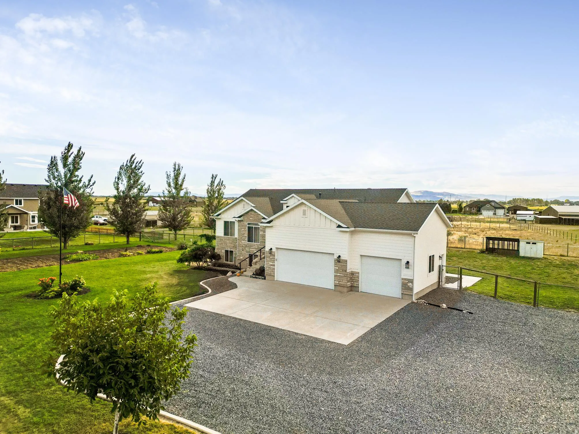 Two-story residence featuring white siding and stone accents, a two-car garage, and an expansive gravel driveway