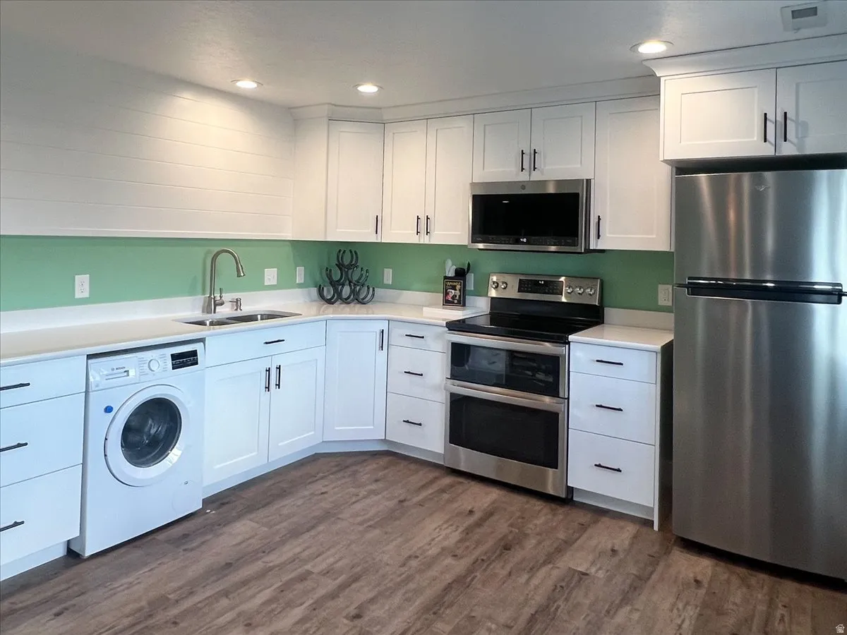 White cabinetry with black hardware, stainless steel appliances, wood-finish flooring, recessed lighting, and a dual basin sink