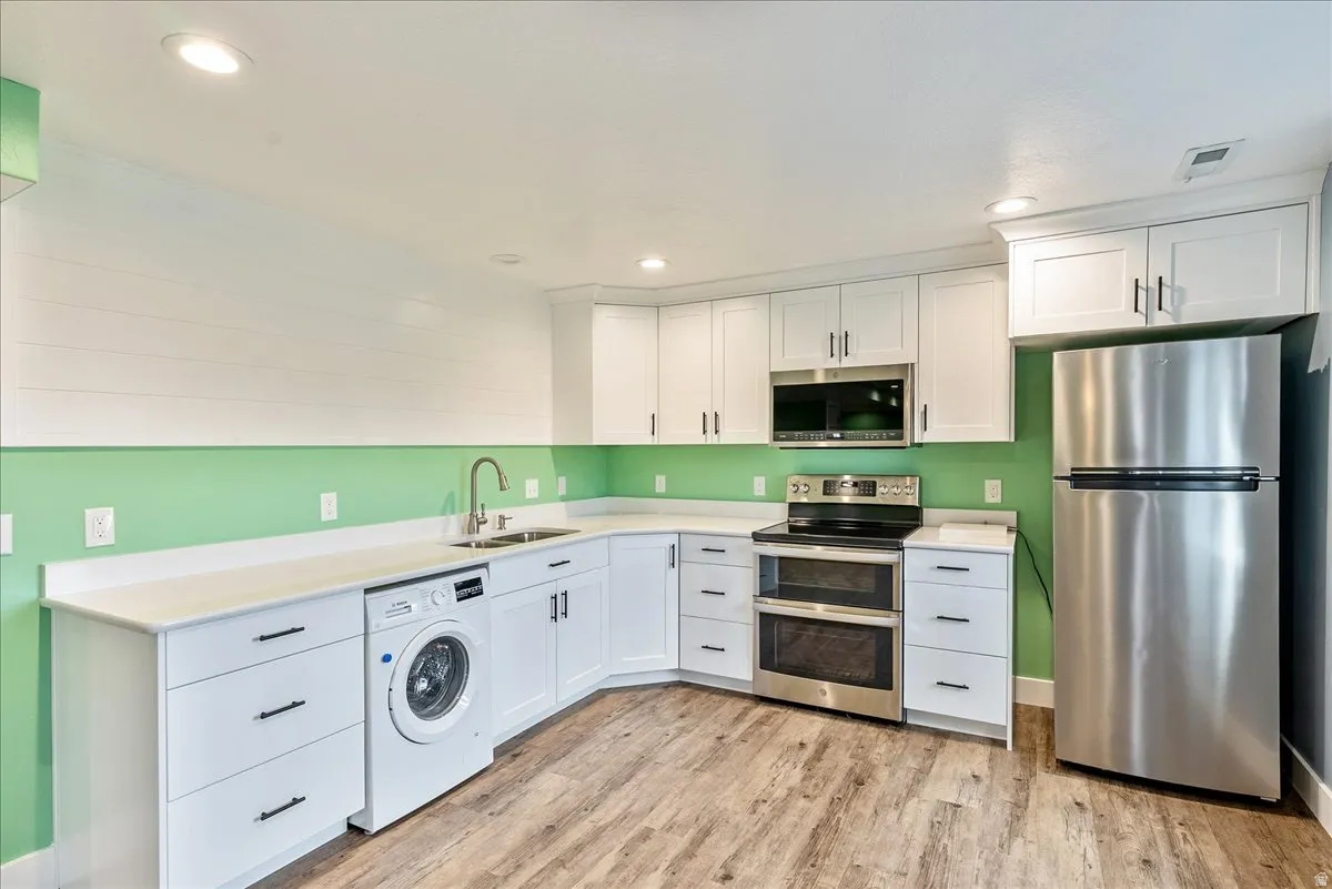 White cabinetry with dark hardware, stainless steel appliances, wood-finish flooring, and recessed lighting