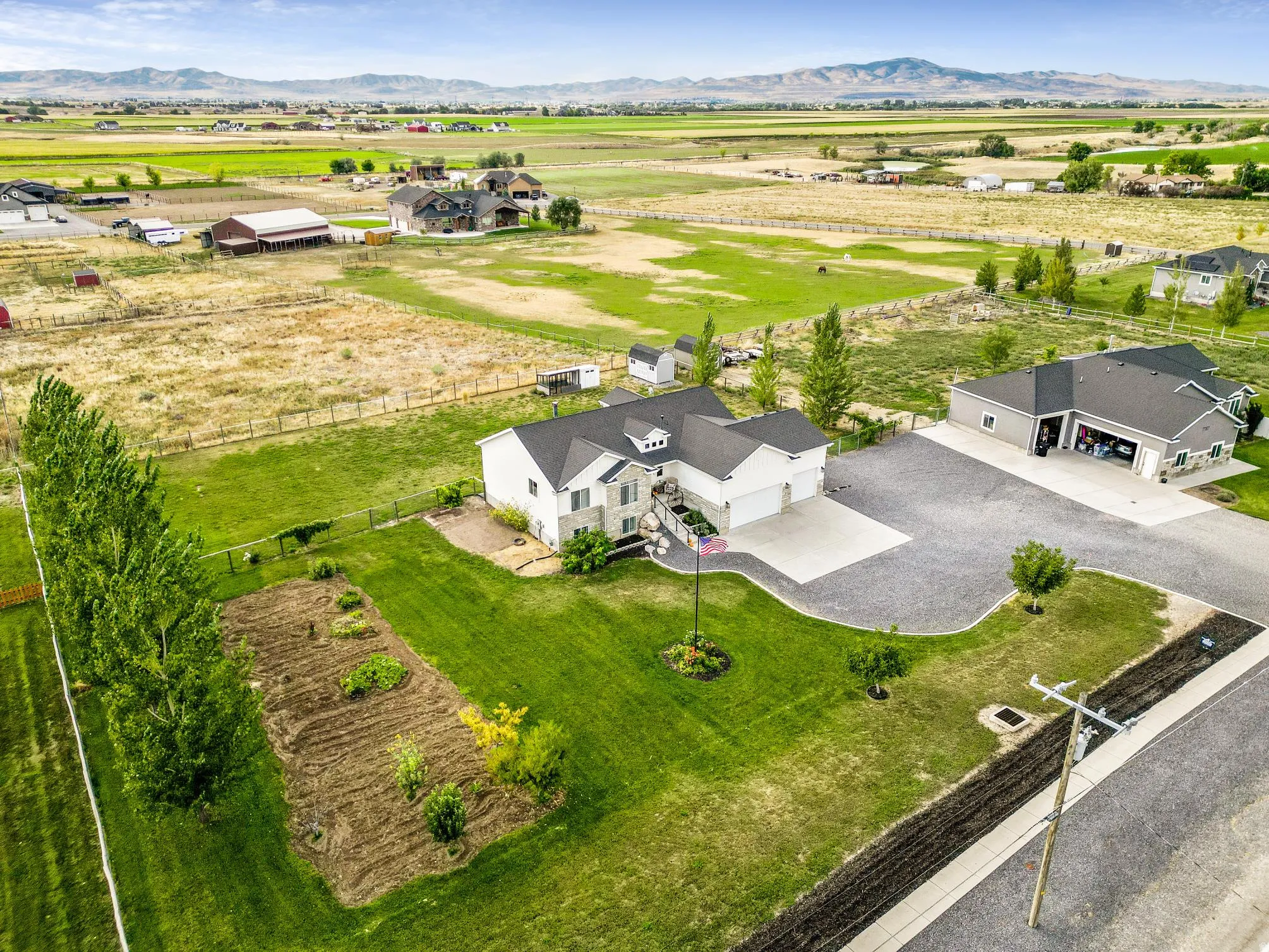 Expansive property featuring a main residence, detached garage, manicured lawn, and a cultivated garden bed