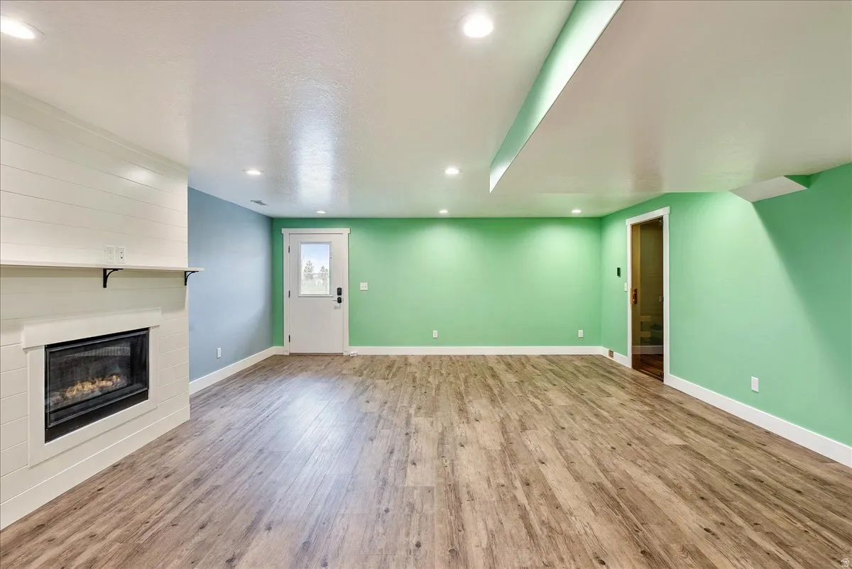Recessed lighting, wood-finish flooring, white shiplap fireplace surround, built-in fireplace, and a light-filled exterior door