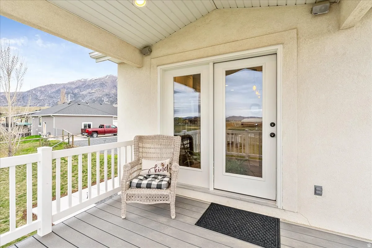 Covered balcony featuring composite decking, white railing, and double French doors with a mountain backdrop