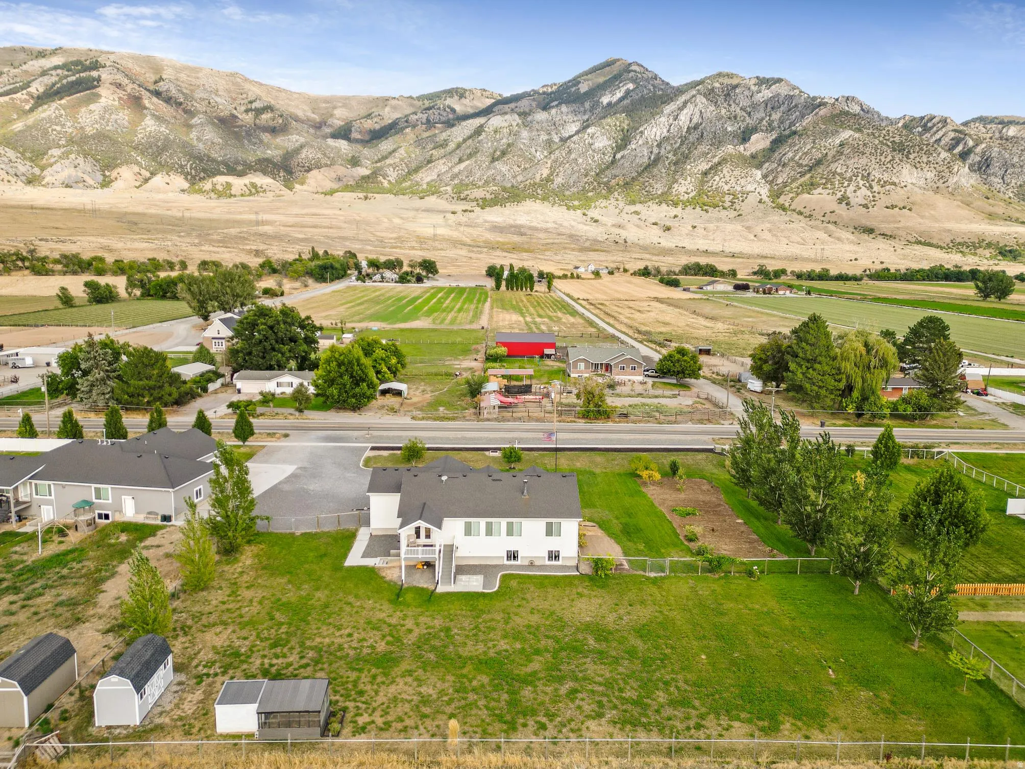 Two-story residence with a rear deck, expansive lawn, and multiple storage sheds