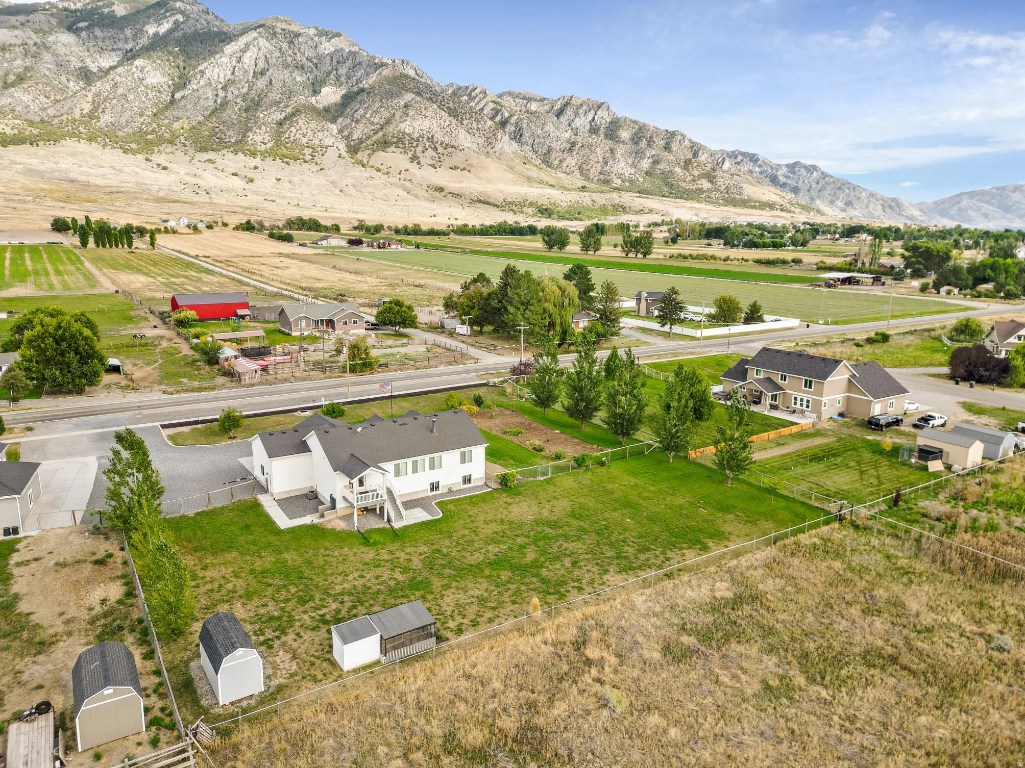 Expansive property featuring a large lawn area, mature trees, mountain backdrop, and multiple outbuildings