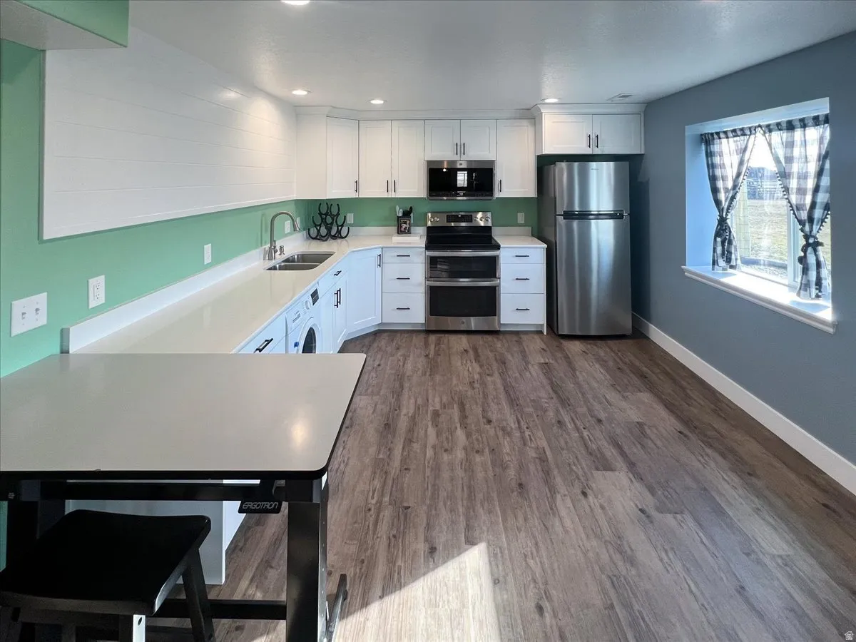 White cabinetry, stainless steel appliances, stone-finish countertops, wood-finish flooring, and a built-in washer unit