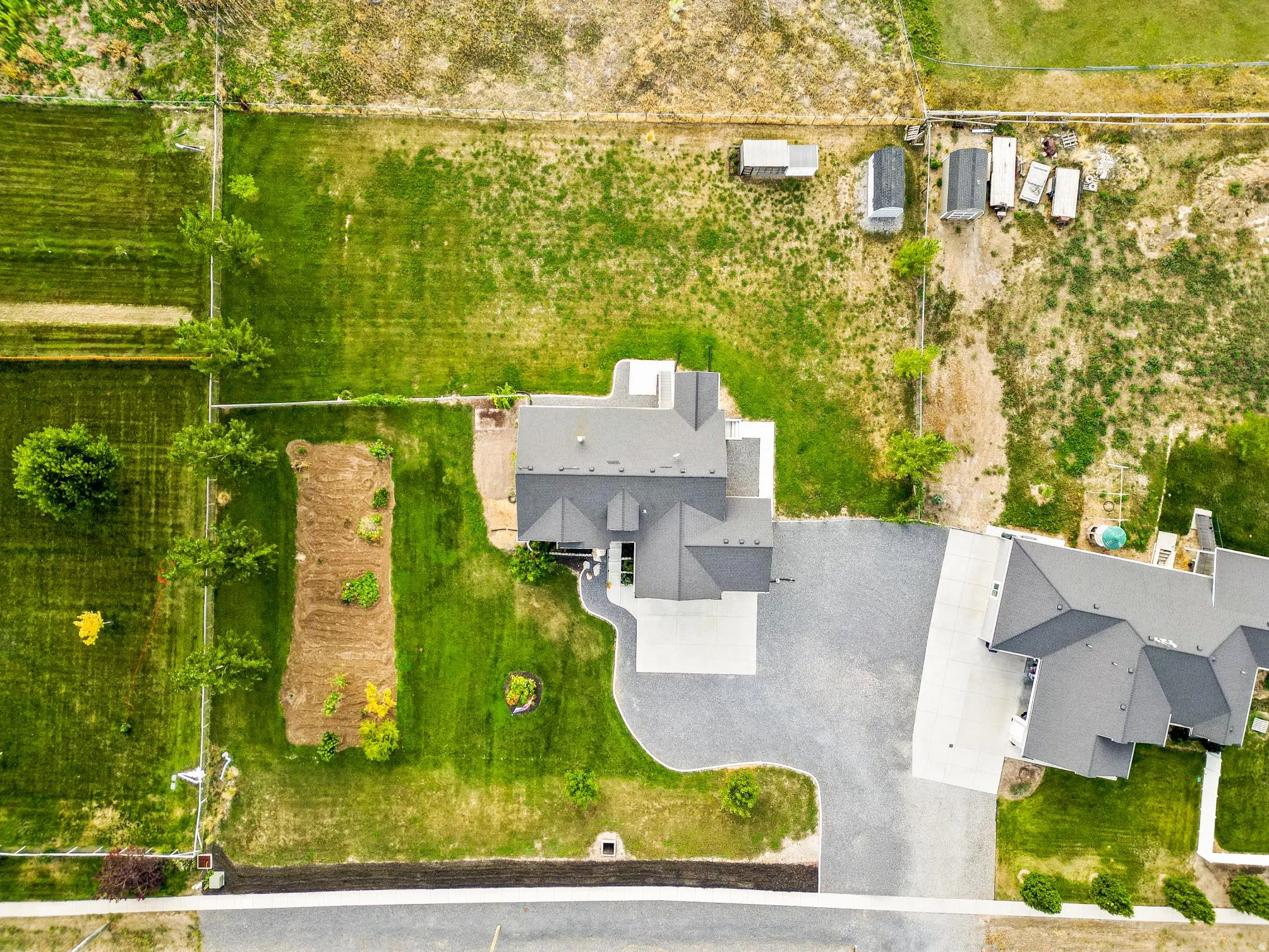 Expansive property featuring a large residence with a multi-gabled roof, extensive paved driveway, established green spaces, and a cultivated garden area