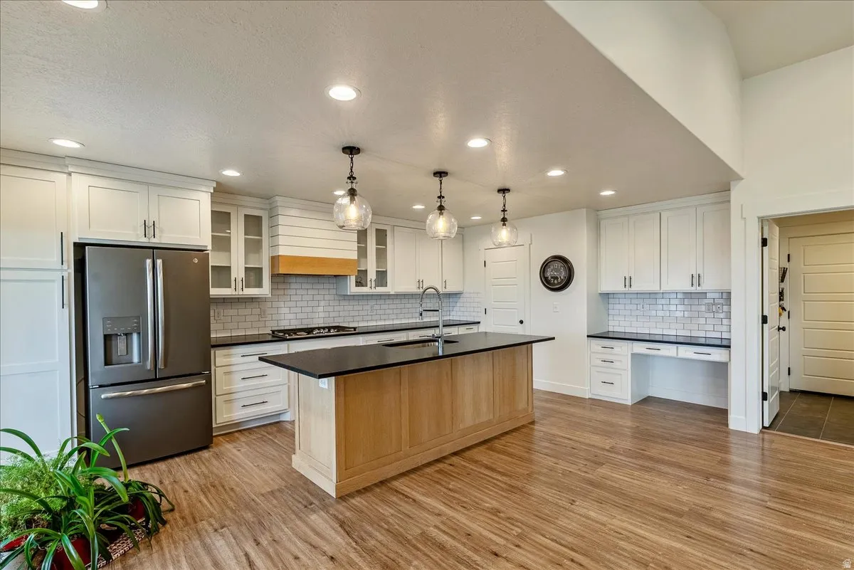 Kitchen featuring wood-finish flooring, recessed lighting, white cabinetry, a central island with a dark countertop, and a built-in desk area