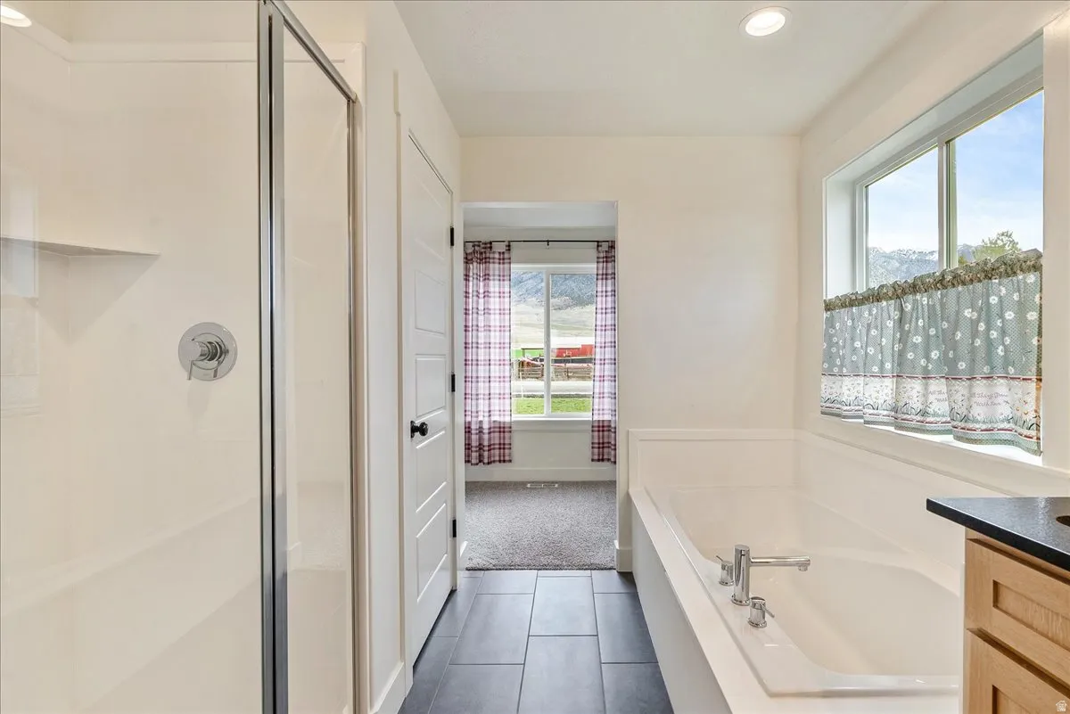 Recessed lighting, a walk-in shower with a chrome fixture, a built-in soaking tub, a window with trim, and black tile flooring