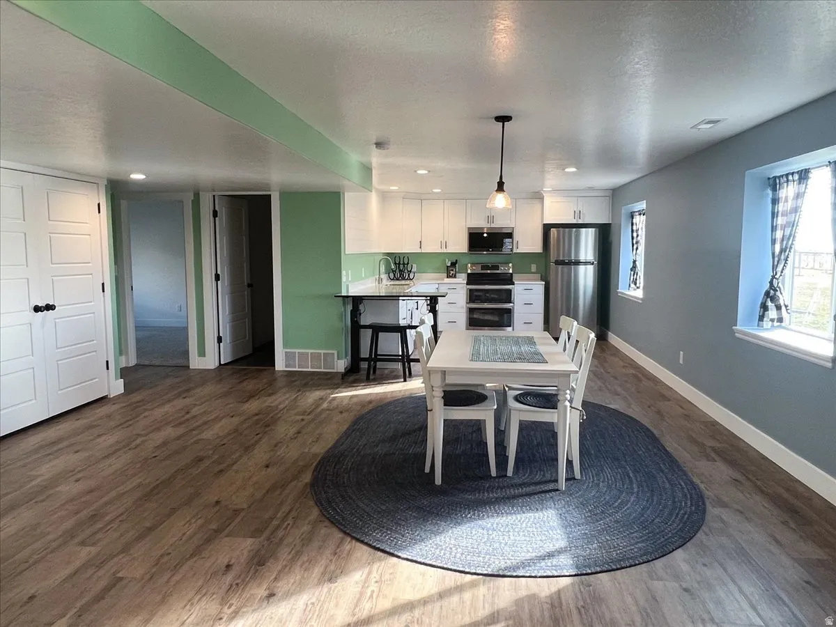 Open-concept living space featuring wood-finish flooring, recessed lighting, a modern kitchen with white cabinetry and stainless steel appliances, and multiple windows allowing natural light