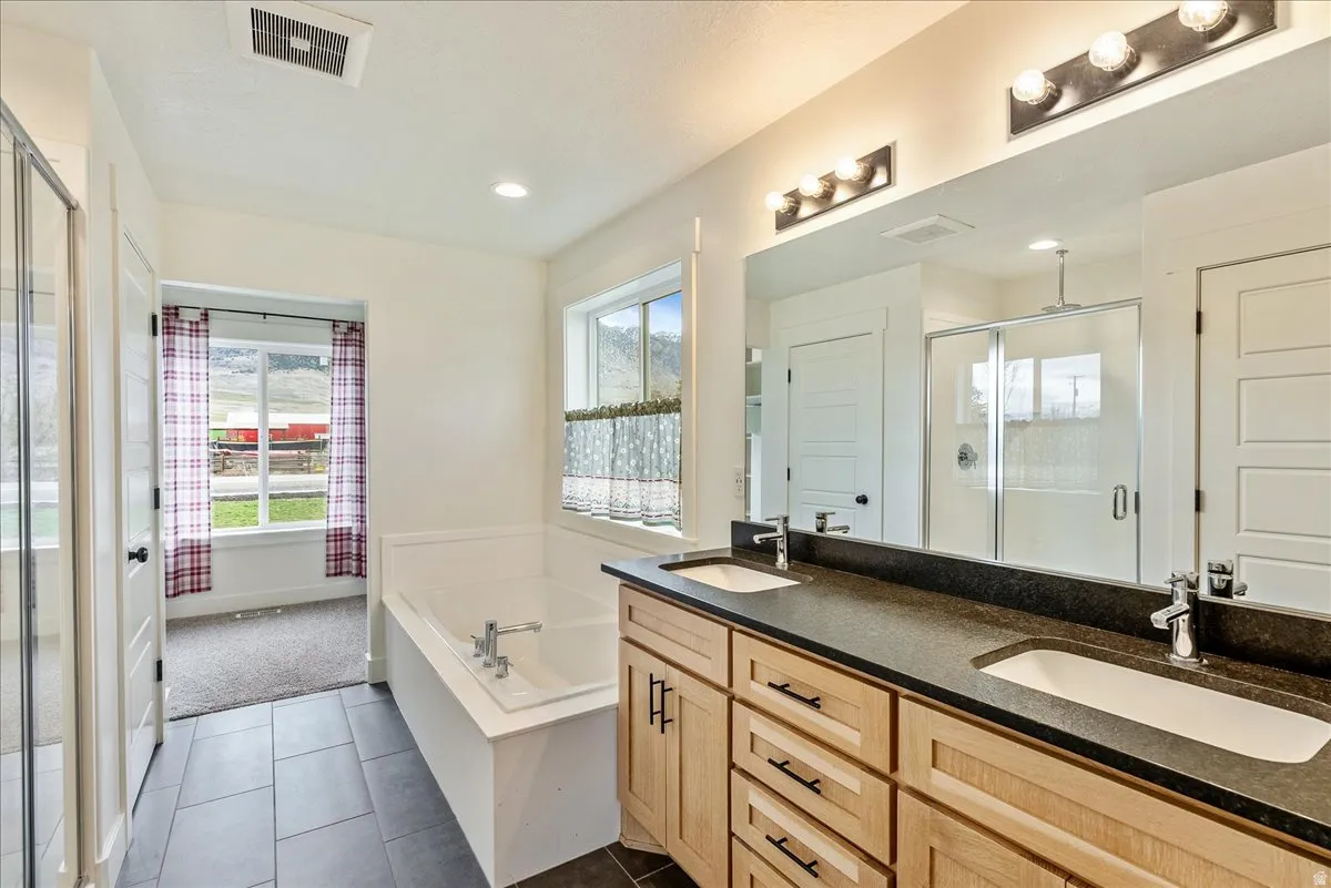 Dual vanity with undermount sinks and dark countertops, wood-finish cabinetry, and a built-in bathtub