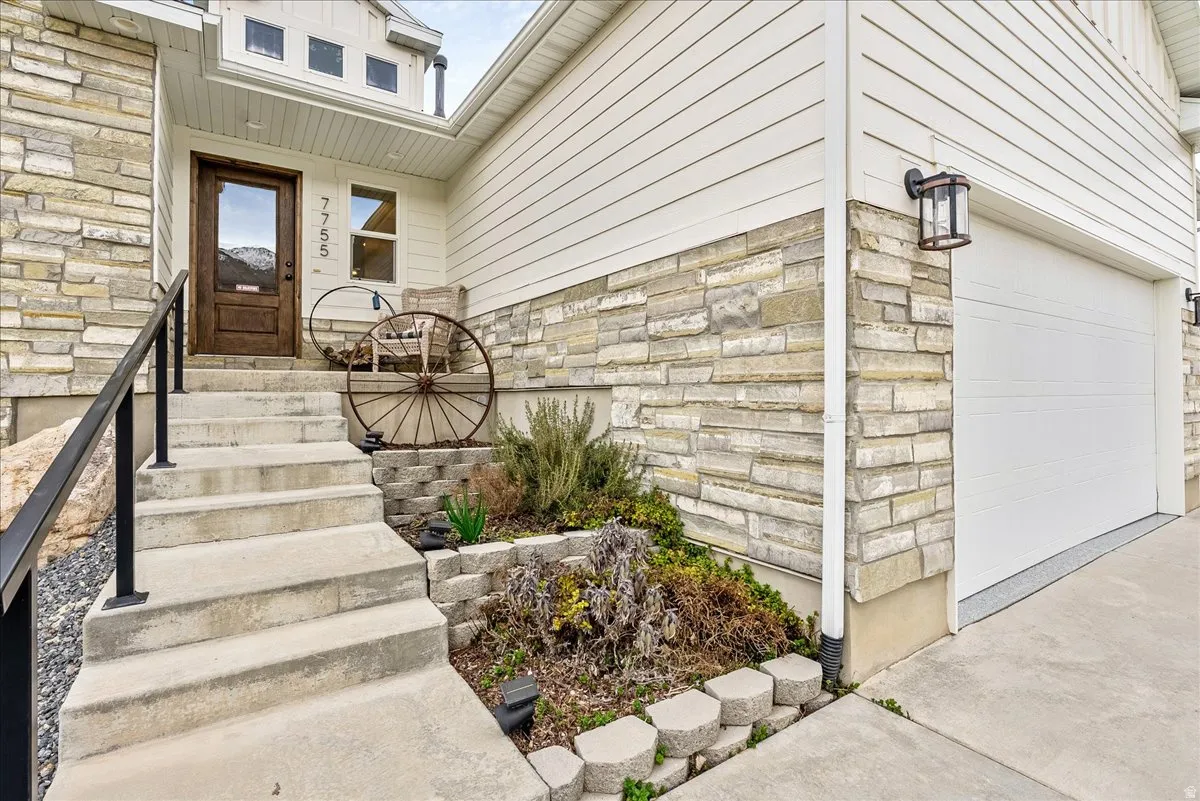 Stone and siding exterior with a wood-finish entry door, concrete steps, and a black metal handrail
