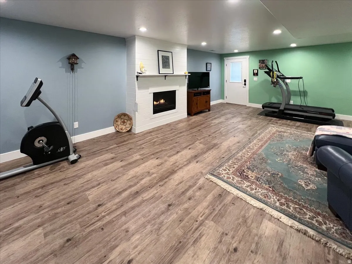Recreational space featuring wood-finish flooring, a built-in electric fireplace with shiplap surround, recessed lighting, and a white paneled door