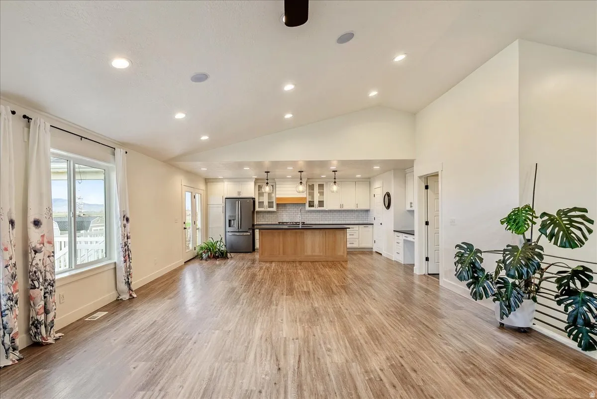 Spacious open-concept interior featuring vaulted ceilings, recessed lighting, wood-finish flooring, and a kitchen with white cabinetry, a wood island, and a dark refrigerator