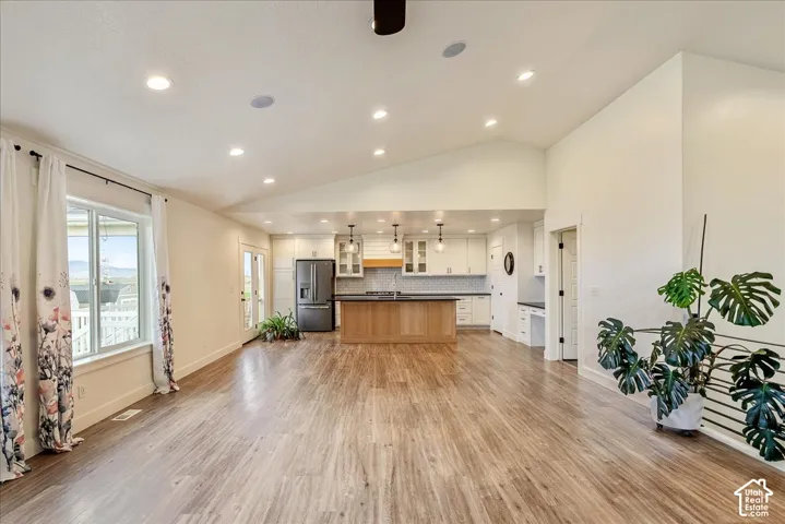 Spacious open-concept interior featuring vaulted ceilings, recessed lighting, wood-finish flooring, and a kitchen with white cabinetry, a wood island, and a dark refrigerator