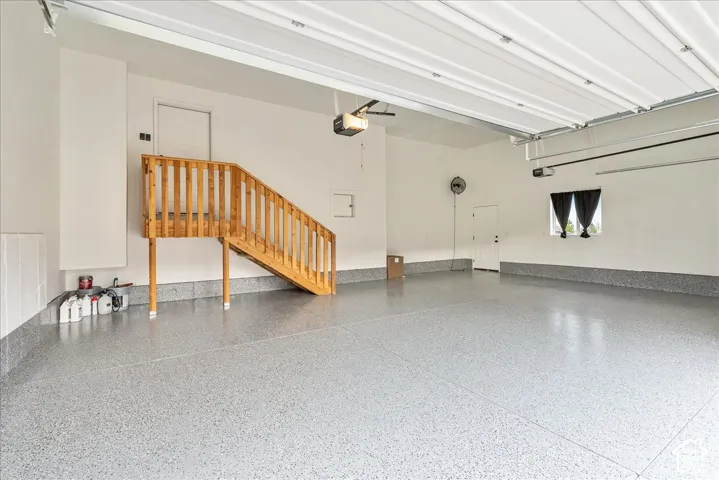 Spacious garage with light-colored, speckled flooring, overhead garage door system, and a natural wood staircase