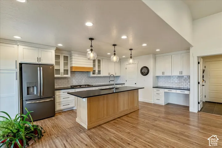 Kitchen featuring wood-finish flooring, recessed lighting, white cabinetry, a central island with a dark countertop, and a built-in desk area