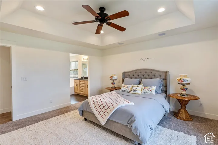 Recessed lighting, ceiling fan, tray ceiling, carpeted flooring, and a bathroom with a wood-finish vanity