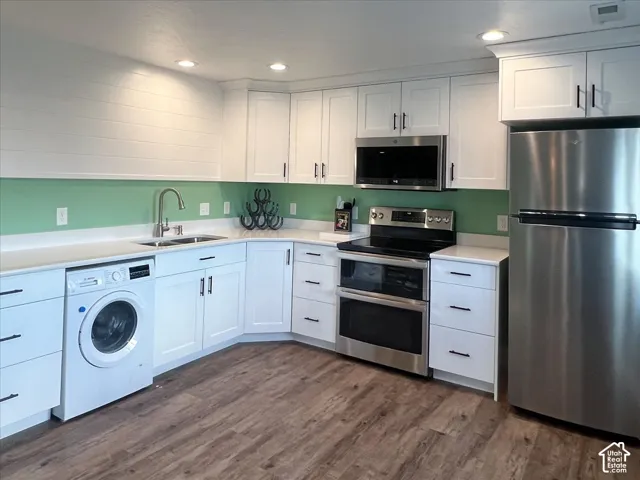 White cabinetry with black hardware, stainless steel appliances, wood-finish flooring, recessed lighting, and a dual basin sink