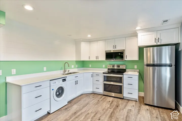 White cabinetry with dark hardware, stainless steel appliances, wood-finish flooring, and recessed lighting