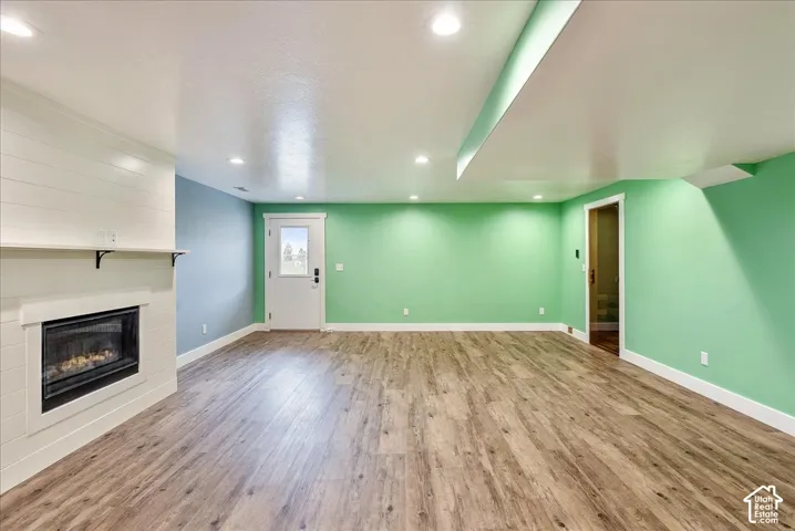 Recessed lighting, wood-finish flooring, white shiplap fireplace surround, built-in fireplace, and a light-filled exterior door