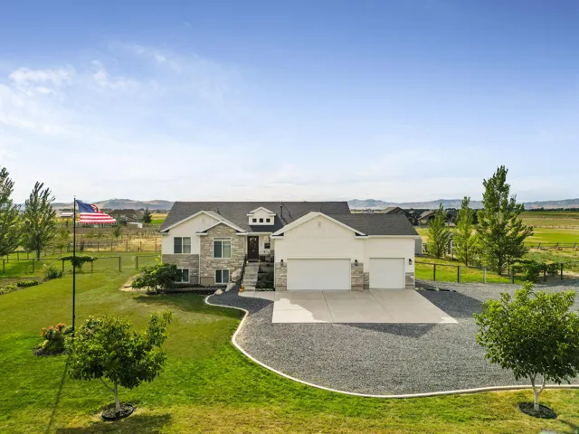 Stone and siding exterior with a two-car garage, gravel driveway, mature trees, and a spacious lawn
