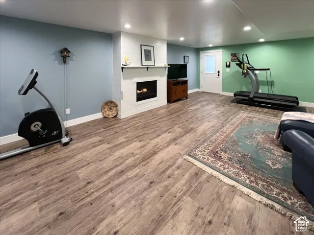 Recreational space featuring wood-finish flooring, a built-in electric fireplace with shiplap surround, recessed lighting, and a white paneled door