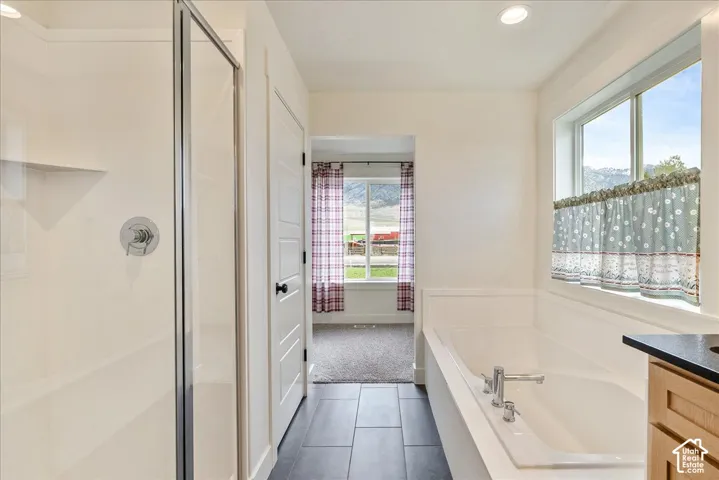 Recessed lighting, a walk-in shower with a chrome fixture, a built-in soaking tub, a window with trim, and black tile flooring