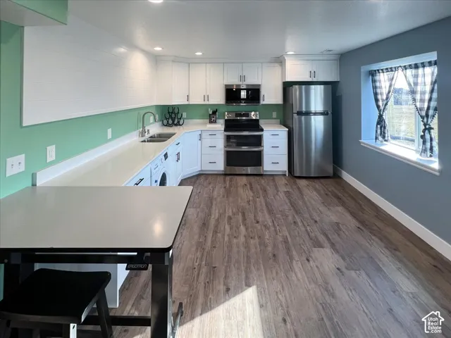 White cabinetry, stainless steel appliances, stone-finish countertops, wood-finish flooring, and a built-in washer unit