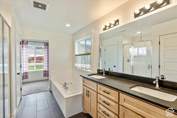 Dual vanity with undermount sinks and dark countertops, wood-finish cabinetry, and a built-in bathtub